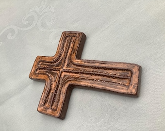 May include: A brown wooden cross with a carved design. The cross is made of wood and has a rustic look.
