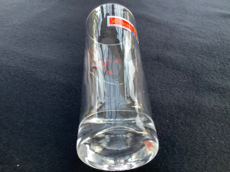 May include: A clear glass drinking glass with a thick base. The glass has a red and blue label with the text "Schott Zwiesel" on it.