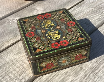 Indonesian tinted square tea tin in a coarse filigree relief print with color areas all around in red, yellow, blue and green.