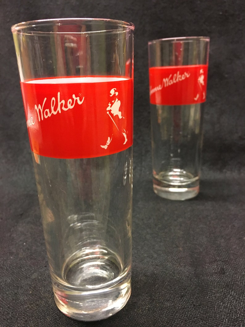 May include: Two clear glass tumblers with a red band and white "Johnnie Walker" logo. The logo includes a stick figure of a man walking with a cane.