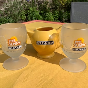 Könnte beinhalten: Zwei Gläser aus mattiertem Glas und ein gelber Krug mit dem Ricard-Logo. Die Gläser tragen die Aufschrift "Feel Sunny" und das Ricard-Logo. Der Krug befindet sich in der Mitte, die Gläser auf beiden Seiten.