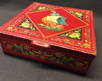 Belle boîte métallique carrée rouge vintage avec l'image en relief d'un vieux voilier et un ornement floral, par 'Coffret Hollandais'