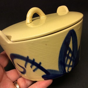 May include: A yellow ceramic covered dish with a blue floral design. The dish has a lid with a handle.