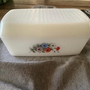 Puede incluir: Caja de pan de cerámica blanca con un diseño floral con flores azules, rojas y blancas. La tapa tiene una superficie texturizada.
