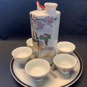 Vintage hand painted ceramic Whistling Bird Sake Set with 5 whistling bottle and cups on a plate. It is painted with Japanese scene, flowers