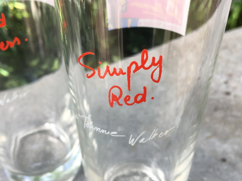 May include: Two clear glass tumblers with the words "Simply Red." written in red ink on one of the glasses. The other glass has the name "Johnnie Walker" written in white ink.