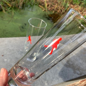 Op de afbeelding: Twee heldere glazen drinkglazen met een rood lopend figuurontwerp aan de zijkant.