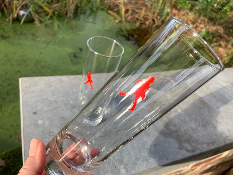 Op de afbeelding: Twee heldere glazen drinkglazen met een rood lopend figuurontwerp aan de zijkant.