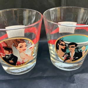 Könnte beinhalten: Zwei klare Glasbecher mit rotem und goldenem Rand. Jeder Becher zeigt eine farbenfrohe Illustration eines Paares in einem gesellschaftlichen Umfeld. Eine Illustration zeigt eine Frau in einem roten Kleid und einen Mann im Anzug. Die andere Illustration zeigt eine Frau in einem blauen Kleid und einen Mann im Anzug.