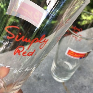 May include: Two clear glass drinking glasses. One glass has the words "Simply Red." written in red cursive on the side. The other glass has a red and blue sticker with the word "Simply" on it.