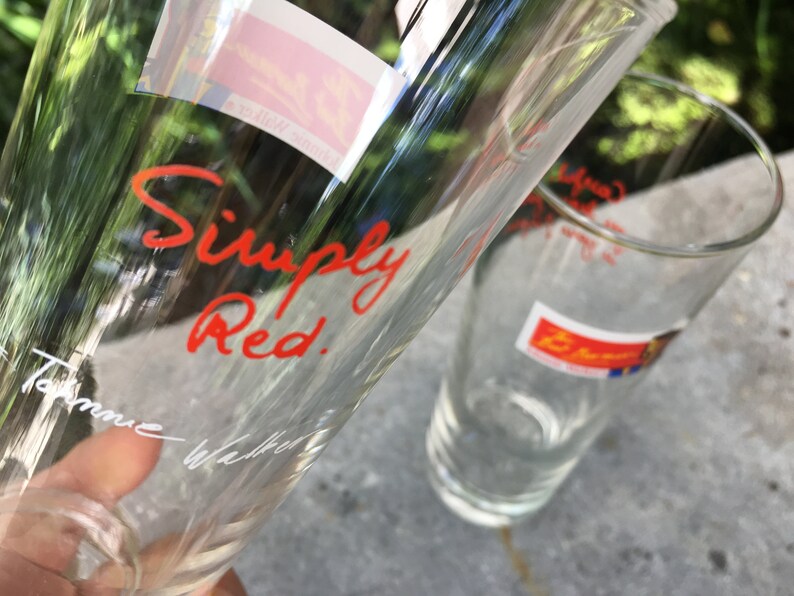 May include: Two clear glass drinking glasses. One glass has the words "Simply Red." written in red cursive on the side. The other glass has a red and blue sticker with the word "Simply" on it.