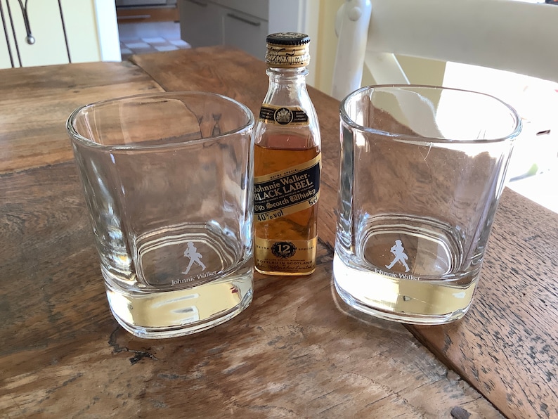 May include: Two clear glass tumblers with the Johnnie Walker logo and a small bottle of Johnnie Walker Black Label Scotch Whisky.