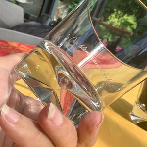 May include: A clear, angled whiskey glass with the etched text "Our blend cannot be beat" is held in a hand. The glass has a unique shape and is partially filled with a clear liquid. A second glass is visible in the background.