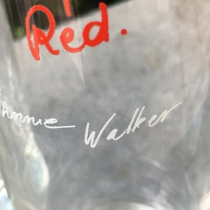 May include: A clear glass bottle with the words "Red." written in red ink and "Johnnie Walker" written in white ink.