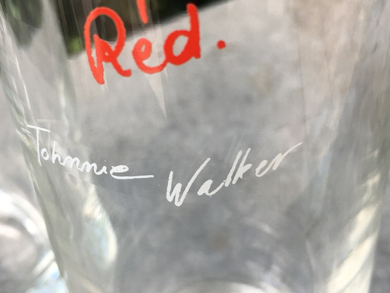 May include: A clear glass bottle with the words "Red." written in red ink and "Johnnie Walker" written in white ink.