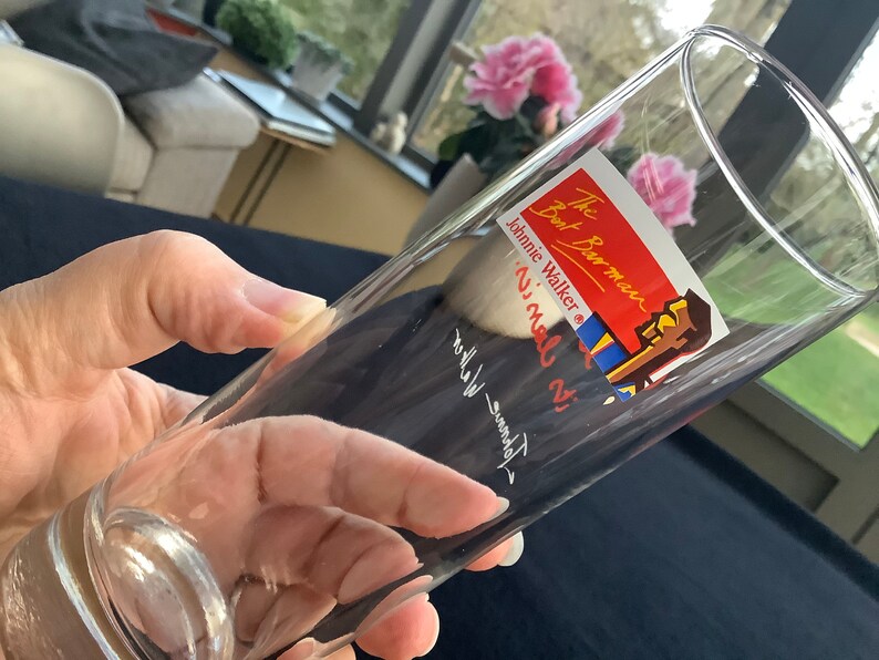 May include: A clear glass with a red and blue sticker that says "The Barman, Johnnie Walker, 'ni' mal di", with a cartoon image of a man in a blue and red shirt.