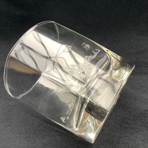 May include: A clear glass tumbler with an etched design of a bird in flight. The glass has a square base and a rounded top.