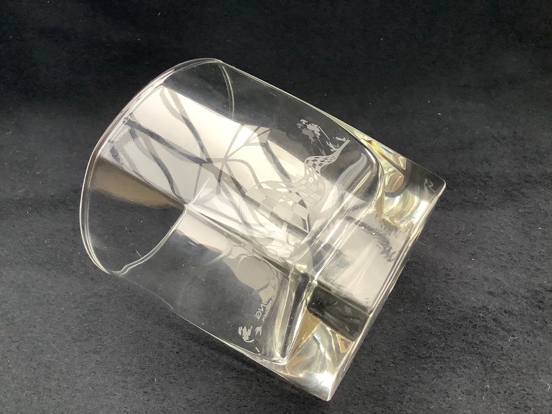 May include: A clear glass tumbler with an etched design of a bird in flight. The glass has a square base and a rounded top.