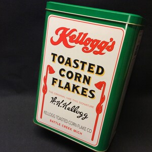 Große rechteckige Dose aus gerösteten Cornflakes, Kellogg's Dose, mit Vintage-Illustration eines Mädchens, das nach Cornflakes auf dem Tisch greift