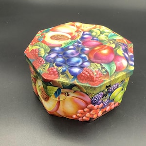Könnte beinhalten: Eine achteckige Metalldose mit einer lebendigen, farbenfrohen Illustration verschiedener Früchte wie Pfirsiche, Trauben, Himbeeren und Brombeeren. Der Deckel und die Seiten sind mit einem detaillierten, realistischen Früchtedesign verziert.