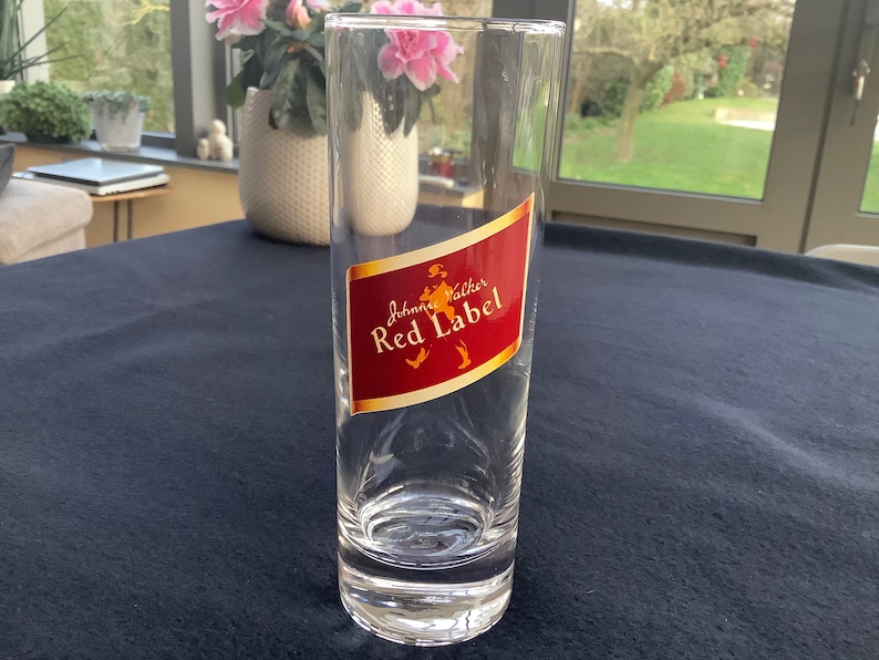 May include: A clear glass tumbler with a red and gold label that says "Johnnie Walker Red Label".