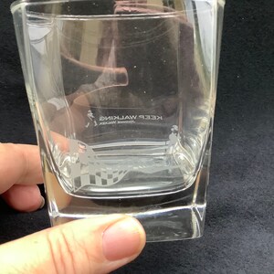 May include: A clear glass tumbler with a square base and etched design. The design features a man walking with a chequered flag and the text "JOHNNIE WALKER KEEP WALKING".