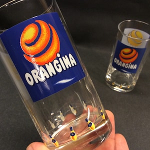 2 vintage orangina-glazen met logo als geschilde sinaasappel en kleine orangina-flesjes aan de onderkant van het glas