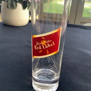 May include: A clear glass with a red and gold label that says "Johnnie Walker Red Label".