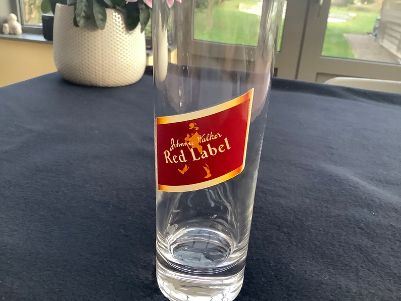 May include: A clear glass with a red and gold label that says "Johnnie Walker Red Label".