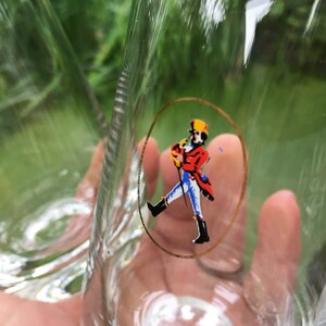 Pu&ograve; includere: Bicchieri di vetro trasparente con un logo bordato d'oro raffigurante una figura che cammina con un cappotto rosso, pantaloni blu e cappello giallo. I bicchieri hanno un design strutturato sul lato.