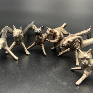 Op de afbeelding: Een verzameling zilverkleurige katten- en hondenbeeldjes. De beeldjes staan in verschillende poses, sommige staan, sommige liggen en sommige interageren met elkaar. De details van de dieren zijn goed gedefinieerd.