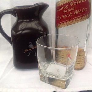 May include: A brown ceramic jug with a Johnnie Walker logo, a clear glass tumbler, and a bottle of Johnnie Walker Red Label Scotch Whisky. The bottle label reads "Johnnie Walker & Sons Ltd., Kilmarnock, Scotland, Produce of Scotland".