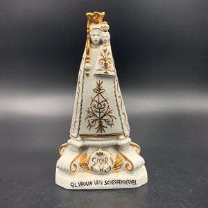 May include: A white ceramic statue of the Virgin Mary and child, with gold detailing. The statue has intricate patterns and the text "Q.VROUW VAN SCHERPENHEUVEL" on the base. The statue is approximately 20 cm tall.