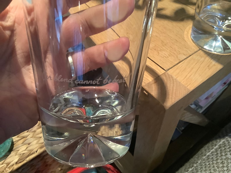 以下が含まれることがあります： 水で満たされた、テクスチャ加工された底を持つ透明なガラス。ガラスには、「Our blend cannot be beat」という文字が側面にエッチングされています。