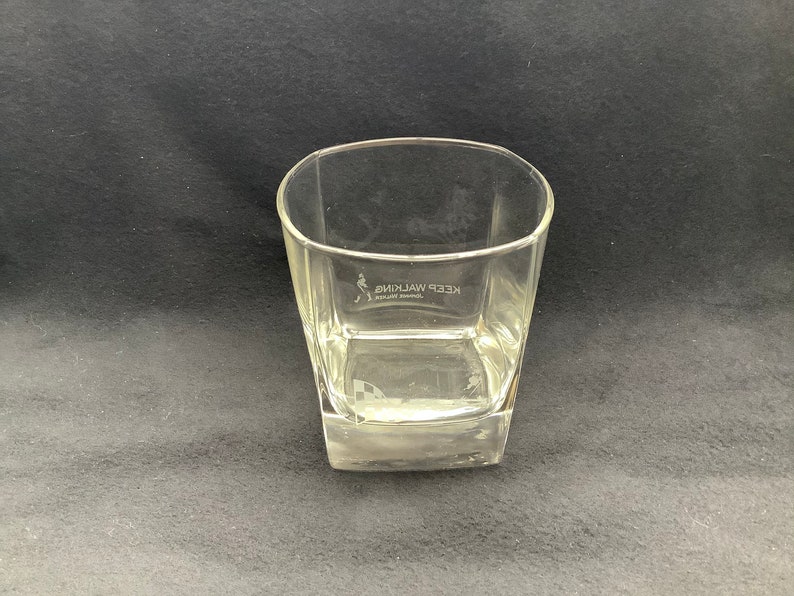 May include: A clear glass tumbler with a square base. The glass has the words "KEEP WALKING" etched on the side.