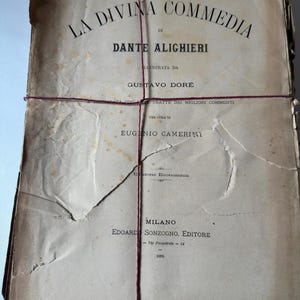 May include: A bundle of old paper pages bound with red string. The top page displays the title "LA DIVINA COMMEDIA" and the author's name, "DANTE ALIGHIERI." The text is printed in black ink on a faded, cream-coloured background. The book is from 1889.