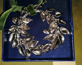 May include: A silver-colored metal holly wreath ornament in a blue velvet box with a green velvet ribbon. The box has a label that reads "Casa d'Arte,  Xilografia,  1994,  15x15cm".