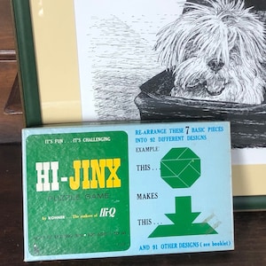 May include: A framed monochrome drawing of a dog in a pram, with a green frame and a cream-coloured mount. Next to it is a vintage Hi-Jinx puzzle game box with text that reads "It's Fun... It's Challenging".