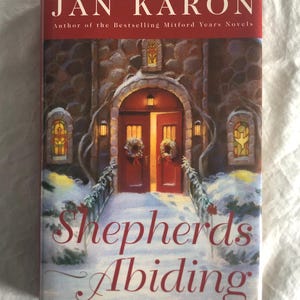 May include: A book cover with a red background and a snowy scene. The title is "Shepherds Abiding" and the author is Jan Karon. The book is about the bestselling Mitford Years novels.