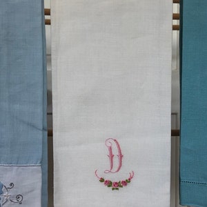 Op de afbeelding: Witte linnen theedoek met een geborduurde roze letter "D" en een krans van roze rozen.