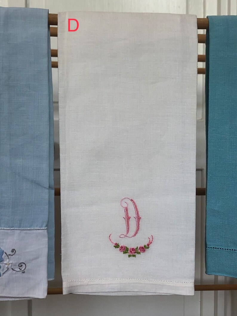 Op de afbeelding: Witte linnen theedoek met een geborduurde roze letter "D" en een krans van roze rozen.