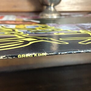 Op de afbeelding: Een zwarte vinylplaat met een geel en zwart ontwerp. De plaat is getiteld "Greg Kihn".