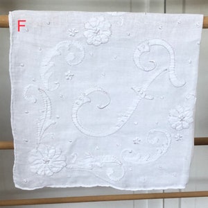 Op de afbeelding: Wit katoenen zakdoek met delicate witte borduursels van een bloemenmotief en de letter "F".