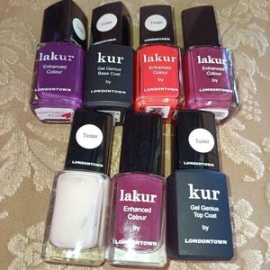 May include: A collection of Londontown nail polish bottles in various colors, including purple, red, and white. The bottles have black caps and white labels that read "Tester". The text "lakur Enhanced Colour" is visible on some bottles.