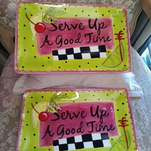 May include: Two rectangular serving platters with a pink background and green border. The platters have a black and white checkered design, a cherry, a lemon, and a palm tree. The text on the platters reads "Serve Up A Good Time".