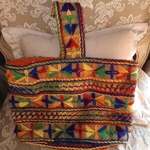 May include: A colorful woven tote bag with a multi-colored embroidered design. The bag has a thick, woven handle.