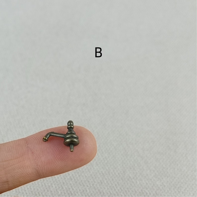 Puede incluir: Un grifo de bronce en miniatura con un dise&ntilde;o decorativo. El grifo est&aacute; en un dedo.