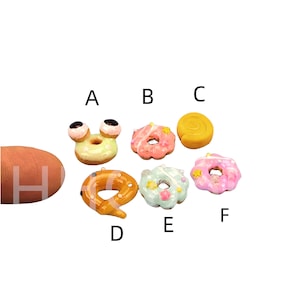 May include: Six miniature donuts with various toppings, including sprinkles, stars, and a swirl design. One donut has googly eyes and a green glaze. The donuts are arranged in a circle on a white background.