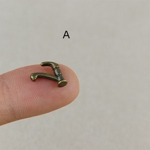Puede incluir: Una peque&ntilde;a figura de grifo de metal de color dorado. El grifo tiene la forma de un grifo de cocina tradicional con un ca&ntilde;o curvo y una manija.