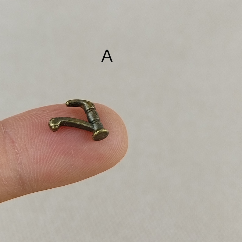 Puede incluir: Una peque&ntilde;a figura de grifo de metal de color dorado. El grifo tiene la forma de un grifo de cocina tradicional con un ca&ntilde;o curvo y una manija.
